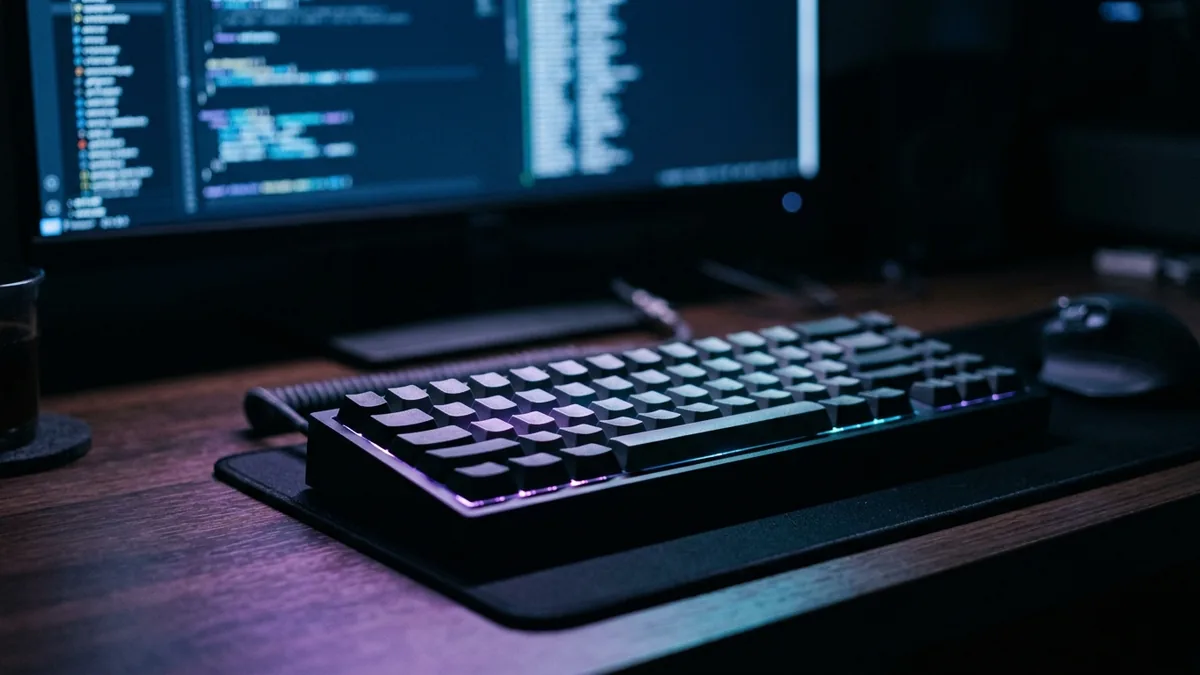 Fotografia em plano detalhe de um teclado mecânico iluminado sobre uma mesa de trabalho em ambiente escuro.